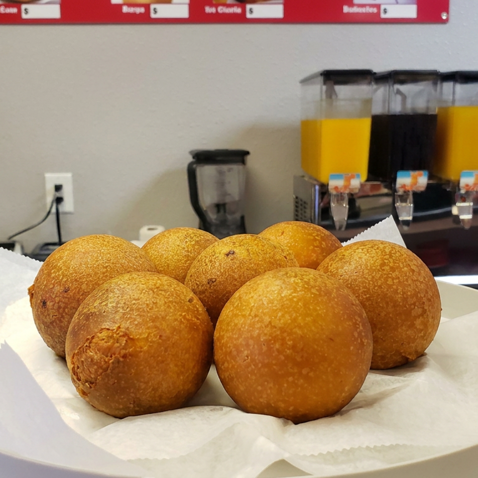 Plate of golden-brown fried dough balls on parchment paper, displayed on a restaurant counter with beverage dispensers behind.