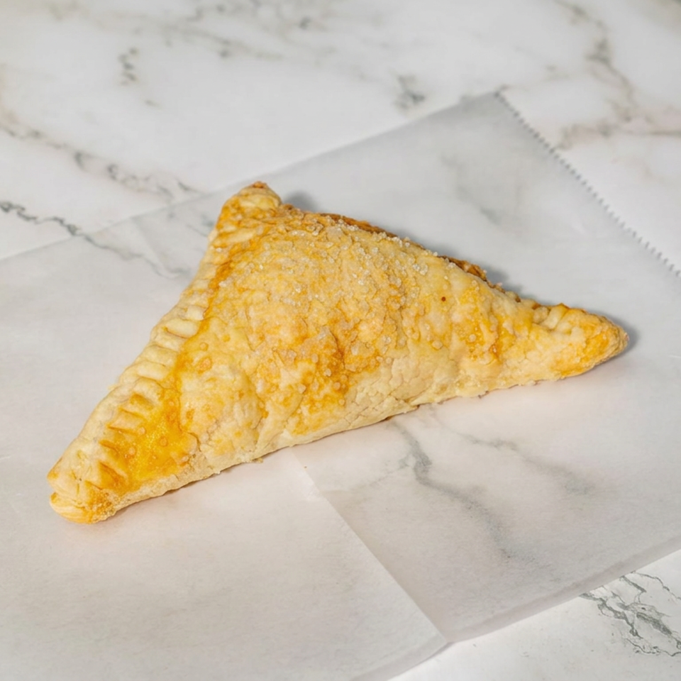 Golden-brown triangular pastry with crimped edges rests on parchment paper atop a white marble surface.